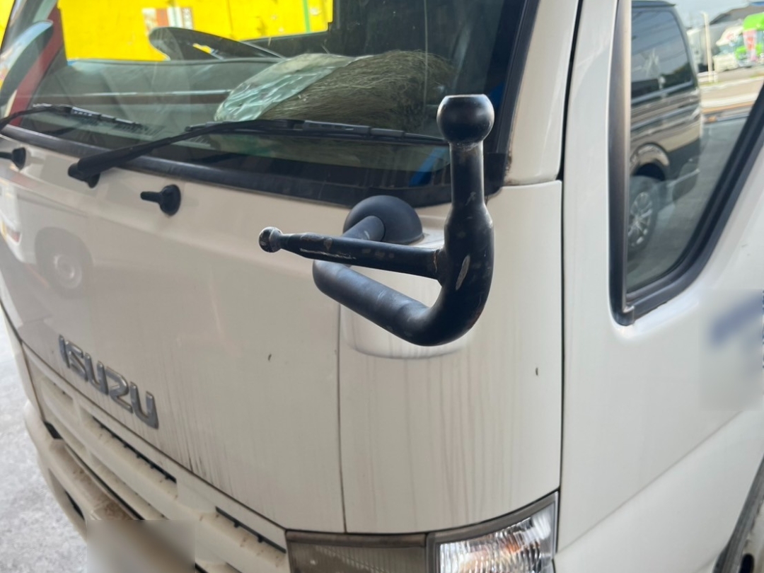 いすゞエルフ左側のサイドミラーが脱落した状態の車両フロント。アーム部分が残り、ミラー本体が無い様子が確認できる。