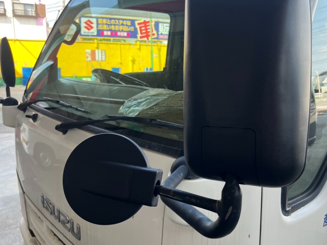 いすゞエルフの左サイドミラーを交換中の様子。大型ミラーと補助ミラーが取り付けられ、工場内で角度調整を行っている。