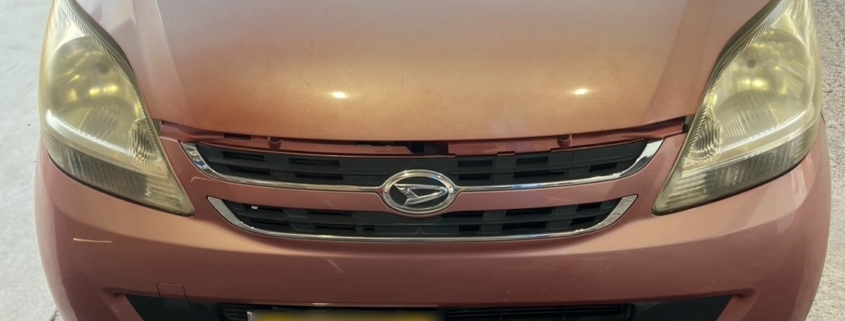 フロントから見たダイハツ ムーヴ（L150系）の外観。経年劣化によりボンネット塗装が退色しており、車体前方の床には液体の漏れ跡が見られる