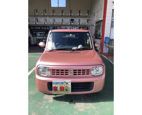 愛知県江南市の整備工場前にて撮影されたスズキ アルト ラパンのピンク色車両。正面からのアングルで“KANAMORI 車検”プレート付き。