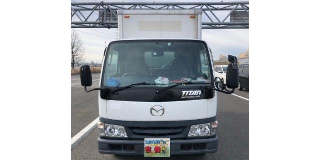 道路上で正面から撮影されたマツダ・タイタンのアルミバントラック。商用利用される中型トラックの外観が分かる画像。